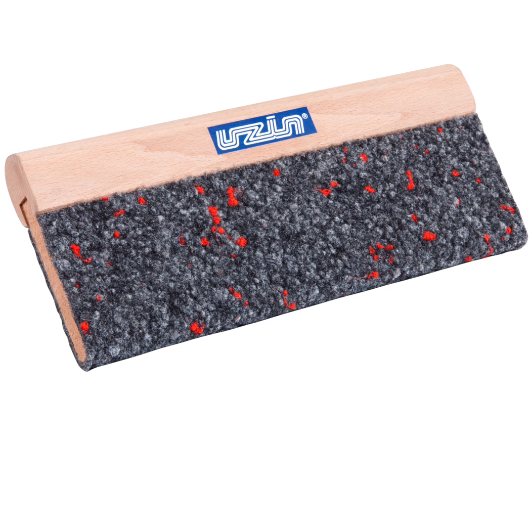 UZIN_Dummy_cork rubbing board textile covered-UZIN_2014-01 Zbliżenie prostokątnego narzędzia z jasnym drewnianym uchwytem i szarą, grubą filcową nakładką, wyszczególnioną małymi czerwonymi włóknami; na gładkim uchwycie z drewna buku widoczna jest mała niebieska etykieta marki. Narzędzie sfotografowano pod kątem na białym tle, co podkreśla fakturę filcu i drobne usłojenie drewna.